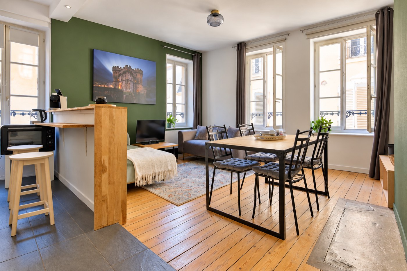 Salon et salle à manger avec mur vert, parquet clair et trois grandes fenêtres